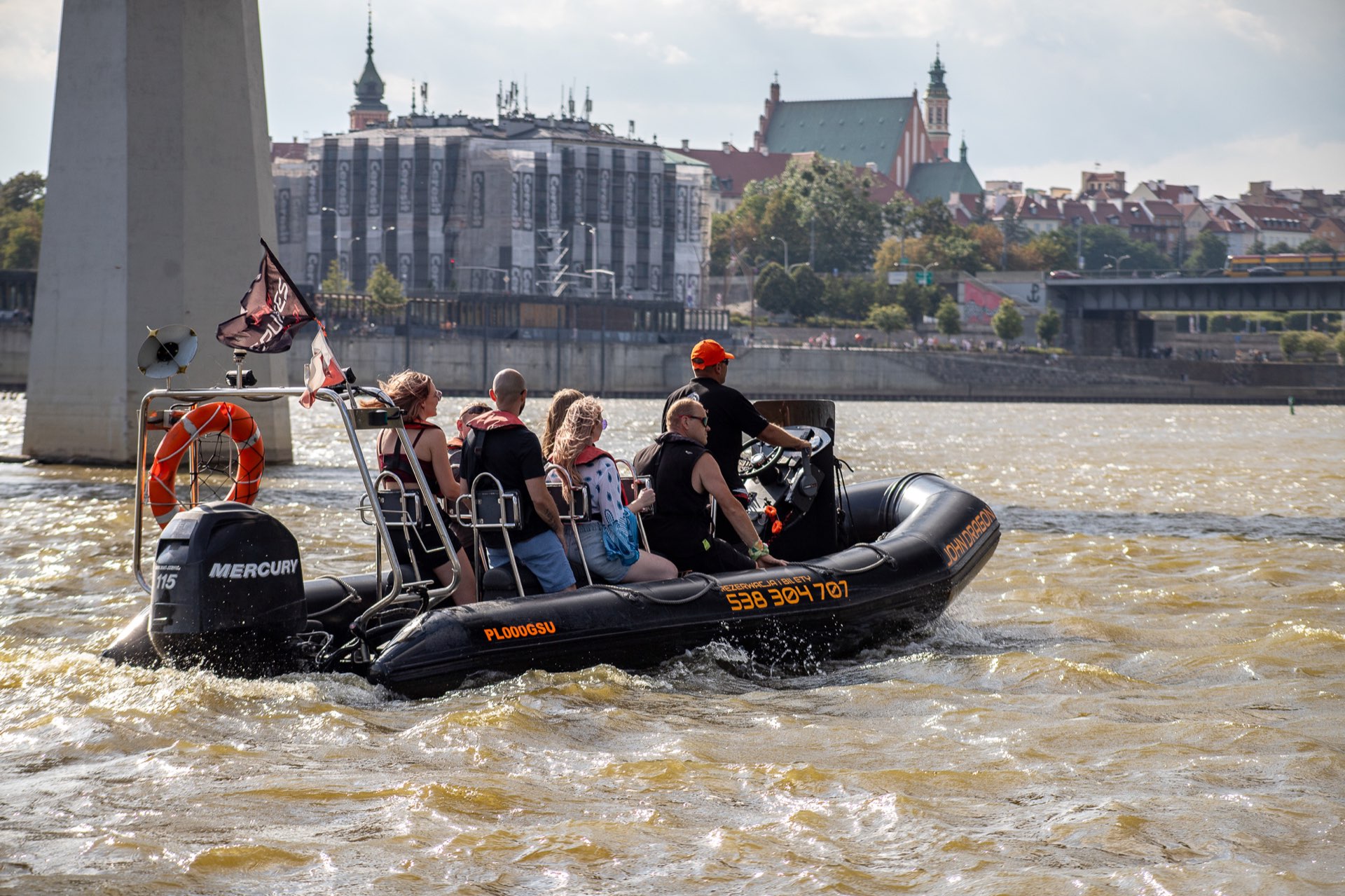 Motorówka John Dragon z grupą pasażerów na Wiśle, w tle sylwetka Starego Miasta w Warszawie