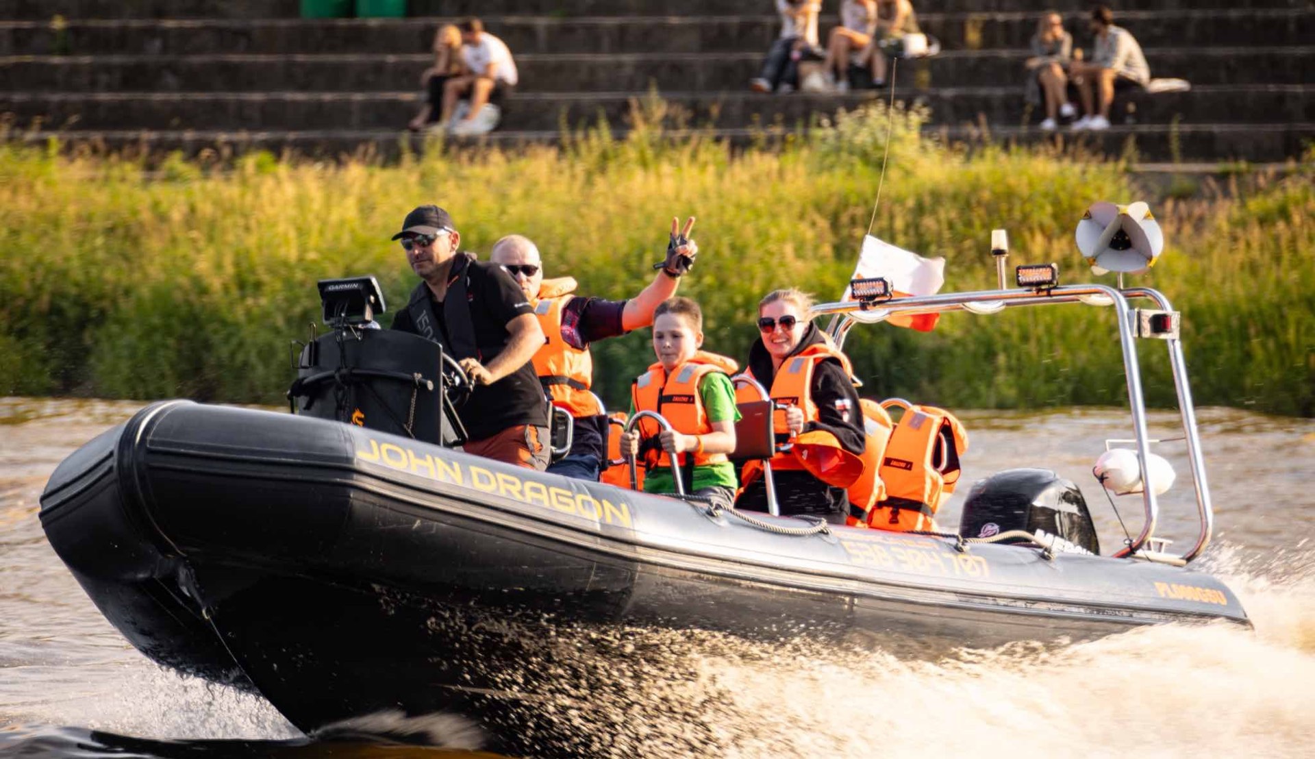Rodzina na pokładzie motorówki RIB John Dragon, chłopiec pokazujący znak zwycięstwa, bryzgi wody, złota godzina